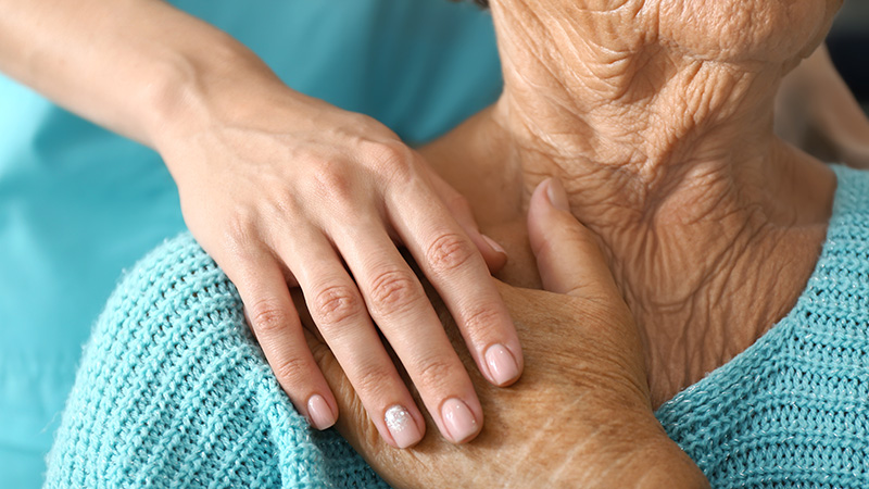 Caregiver gently placing a hand on a senior resident's shoulder in a gesture of comfort and support