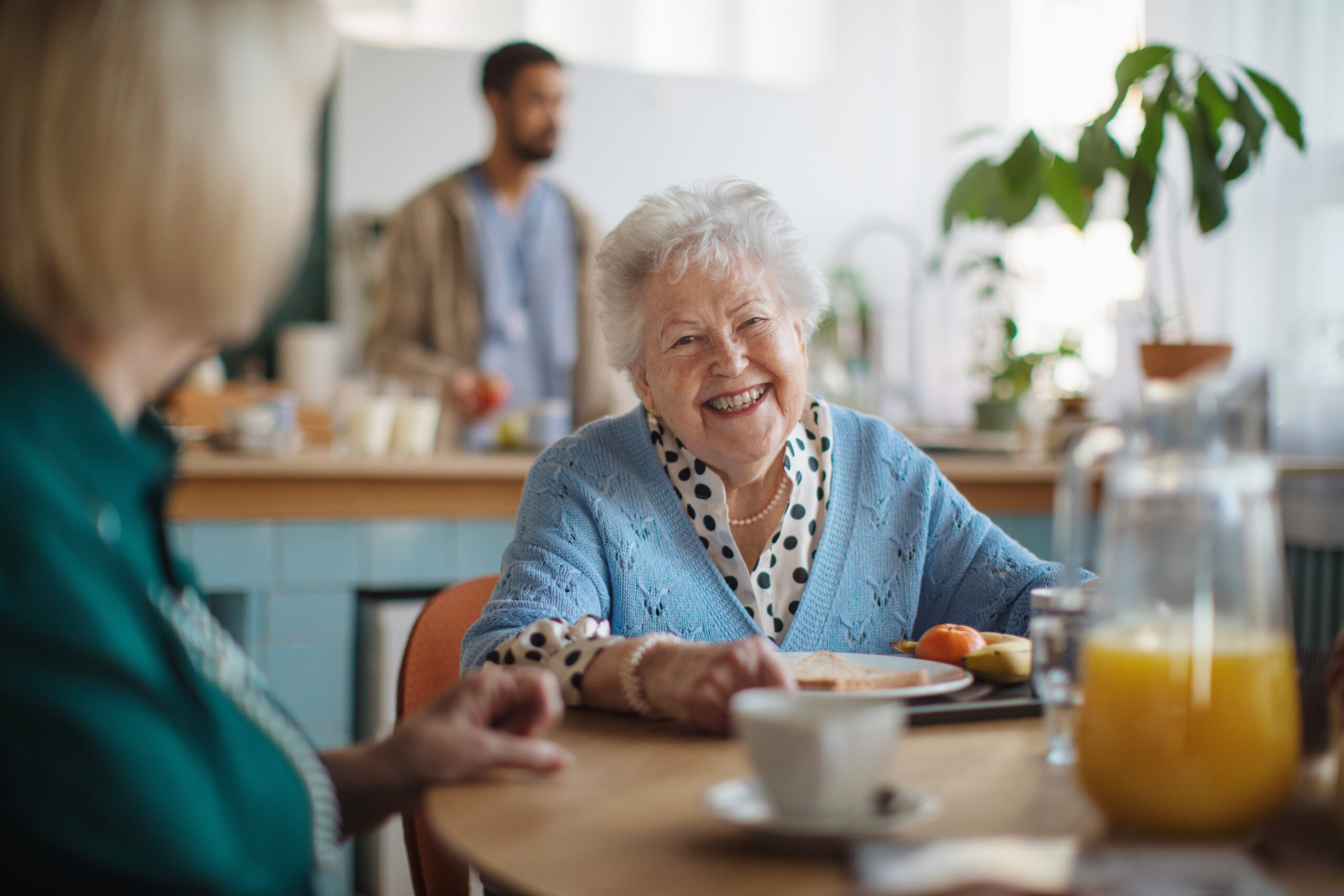 Senior resident laughing with a friend over breakfast in a shared dining are