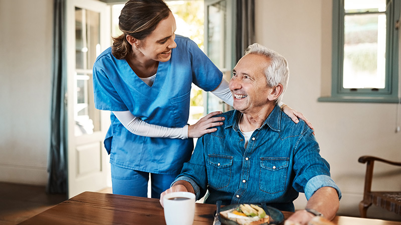 Caregiver checking in on a smiling resident during mealtime at Cornerstone Residence of Oklee