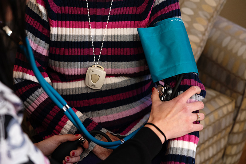 Close-up of a blood pressure check and personal emergency call pendant during a resident wellness check